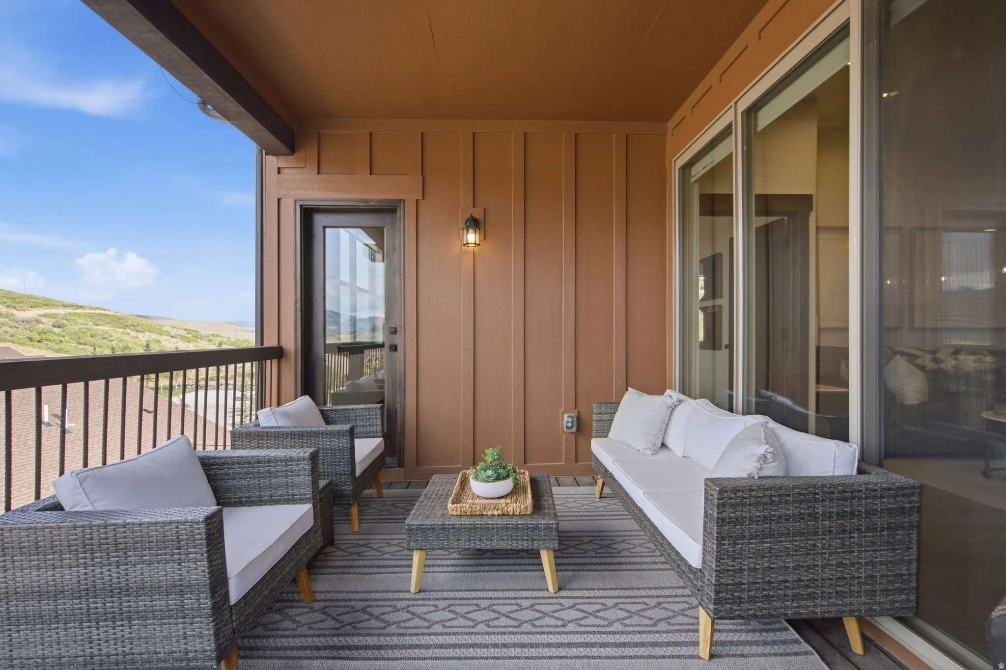 Covered outdoor patio with wood-finish ceiling, vertical panel siding, exterior wall light, glass-paneled door, and sliding glass doors