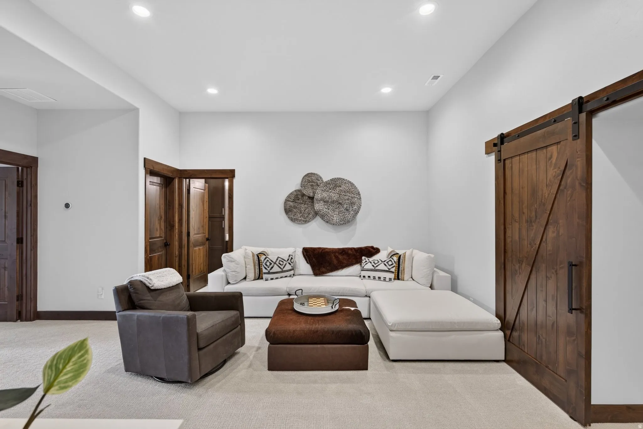 Recessed lighting, wood-finish interior doors with dark hardware, a wood-finish barn door, and light-toned carpeting