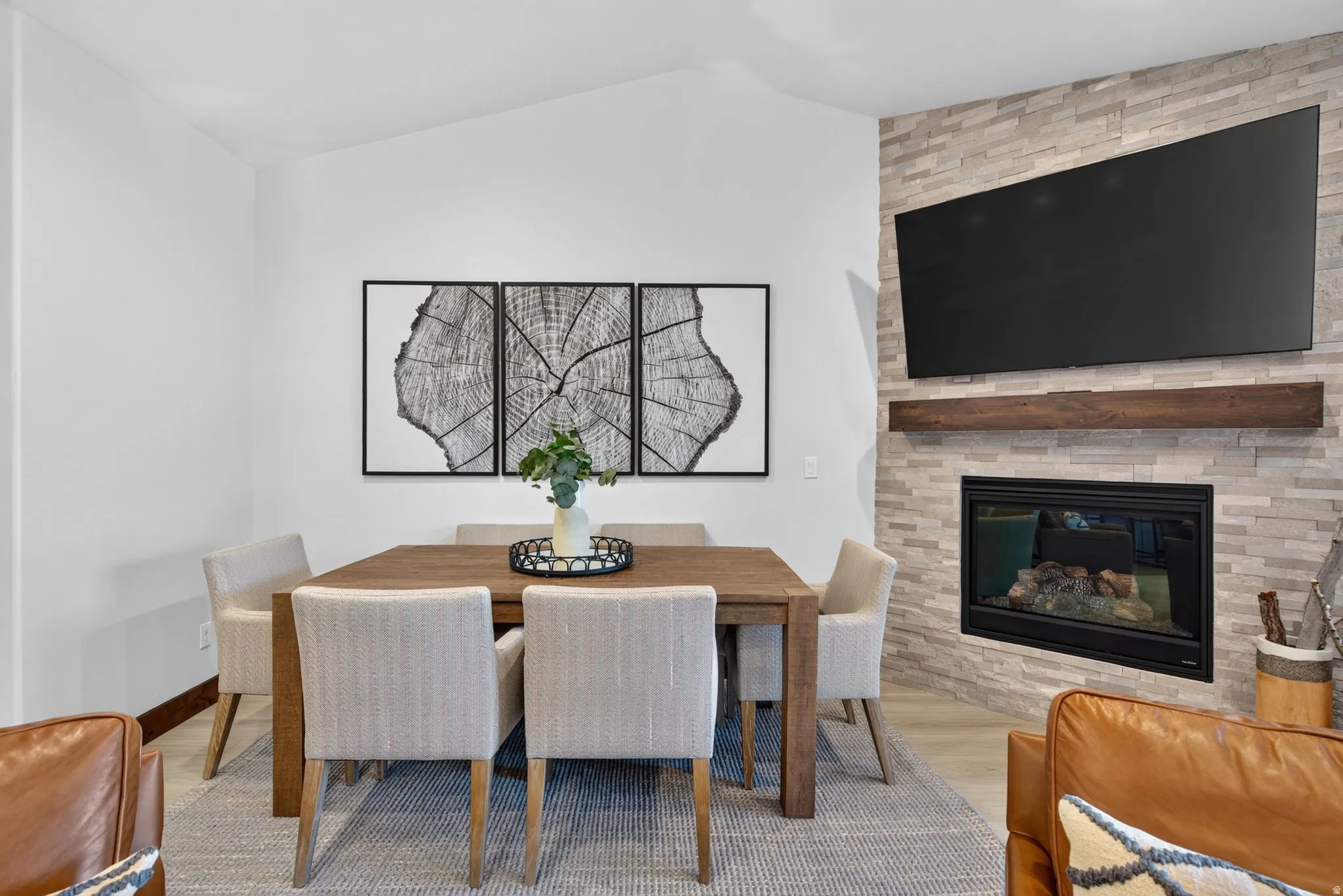 Vaulted ceiling with recessed lighting, stone-clad fireplace, wood mantel, and wood-finish flooring