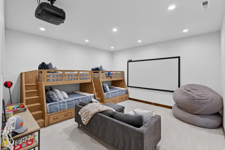 Integrated projector and screen, recessed ceiling lighting, light-toned carpeting, built-in bunk beds with storage drawers, and light wood-finish built-in steps