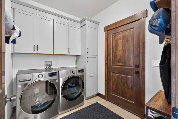 White shaker-style cabinetry with matte black hardware, wood-finish flooring, and a dark wood-paneled door