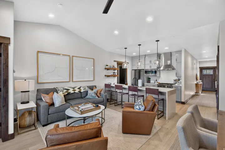 Open-concept living space featuring vaulted ceilings, light wood-finish flooring, a kitchen island with seating, and stainless steel appliances