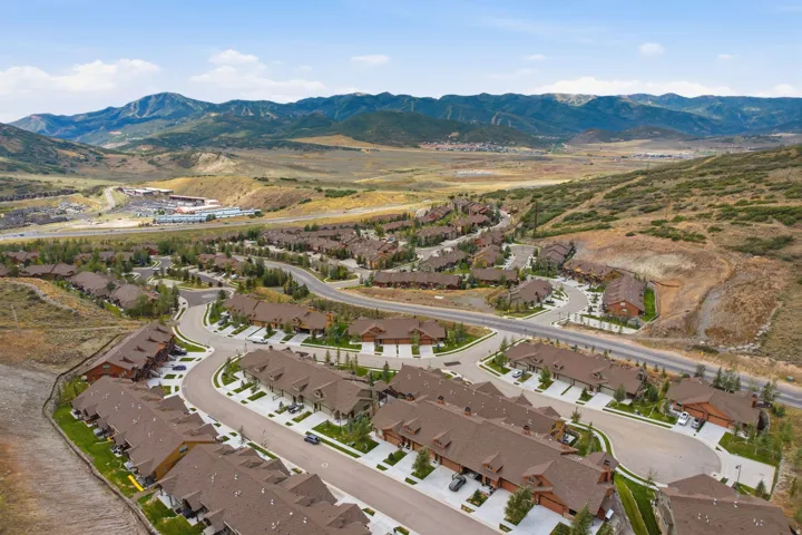 Community of residences featuring brown shingle roofs, paved roadways, and green landscaping, surrounded by a natural mountain backdrop