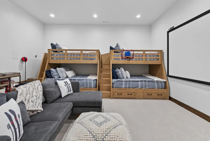 Carpeted recreation room featuring recessed lighting, a large projection screen, and two built-in bunk beds with integrated storage drawers