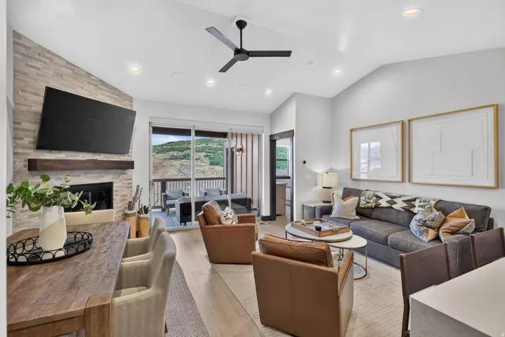Vaulted ceiling with recessed lighting and a ceiling fan, stone-front fireplace with a wood mantel, wood-finish flooring, and a glass sliding door to the exterior