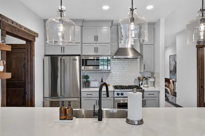 Integrated stainless steel appliances, light gray cabinetry, and a textured subway tile backsplash