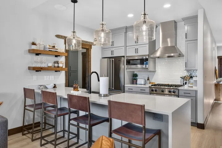 Spacious kitchen featuring a large island, stainless steel appliances, light gray cabinetry, a tile backsplash, and three pendant lights