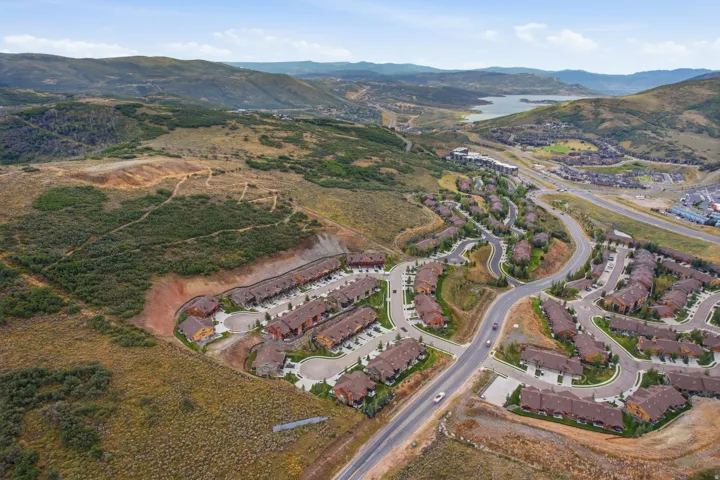 Expansive mountain terrain with a visible body of water, featuring a developed residential area with multiple buildings, paved roadways, and natural landscaping