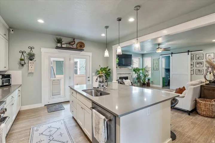 Kitchen featuring a large island with an integrated sink, pendant lighting, white cabinetry, wood-finish flooring, and double glass-paneled doors