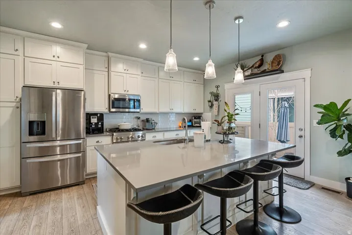 Kitchen with white shaker cabinetry, stainless steel appliances, a center island with pendant lighting, and wood-finish flooring