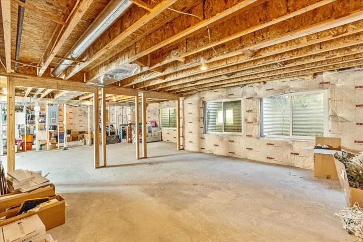 Unfinished basement with exposed ceiling joists, concrete flooring, two rectangular windows, and framed interior walls
