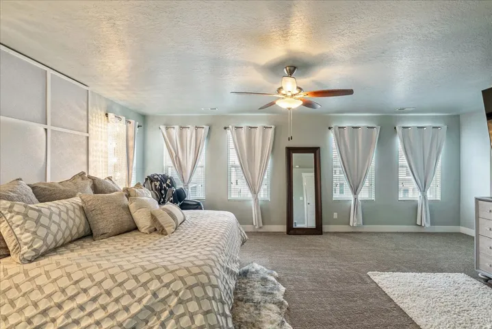 Expansive room featuring carpeted flooring, multiple windows, a ceiling fan with integrated lighting, and a paneled accent wall
