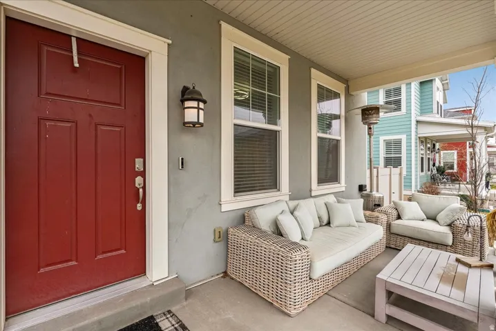 Covered concrete porch with a red paneled entry door, an exterior wall sconce, and white-framed windows