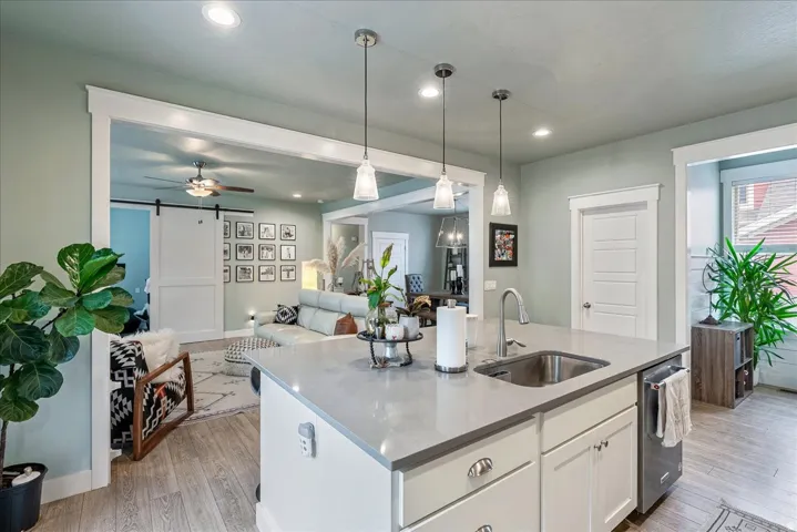 Kitchen island with integrated sink, pendant lighting, recessed lighting, wood-finish flooring, and white cabinetry