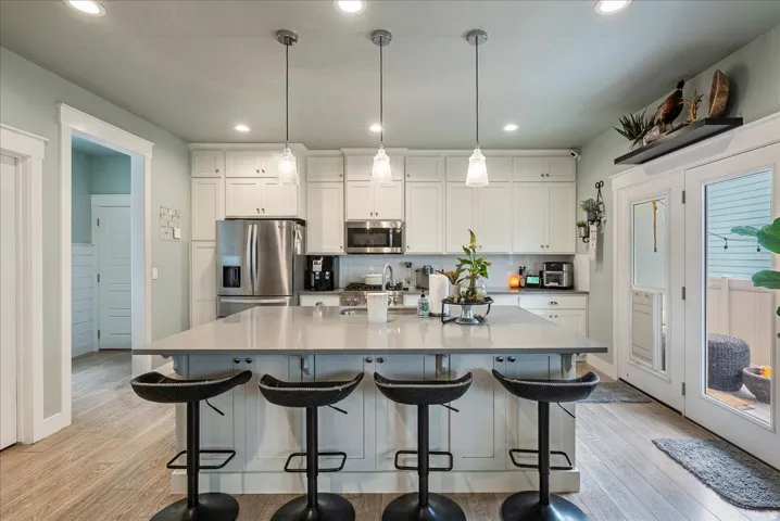 Kitchen featuring white cabinetry, stainless steel appliances, a center island with seating, pendant lighting, and wood-finish flooring