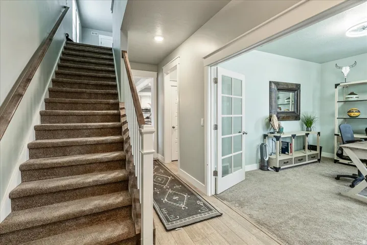 Carpeted staircase with wood-finish handrails, wood-finish flooring, and a room with French doors