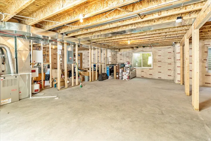 Spacious unfinished basement with exposed beam ceiling, concrete flooring, and framed wall sections ready for customization