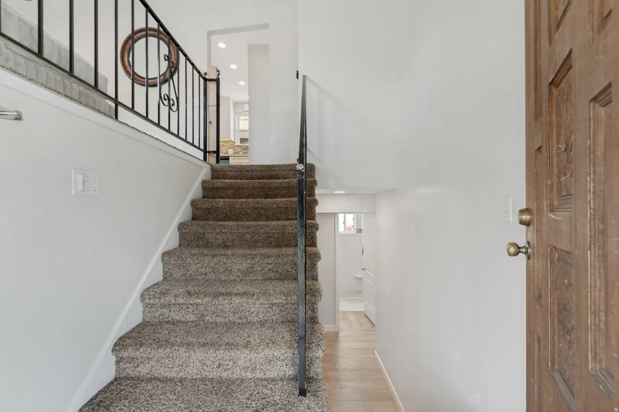 Carpeted staircase with wrought iron railing, leading to an upper level with recessed lighting