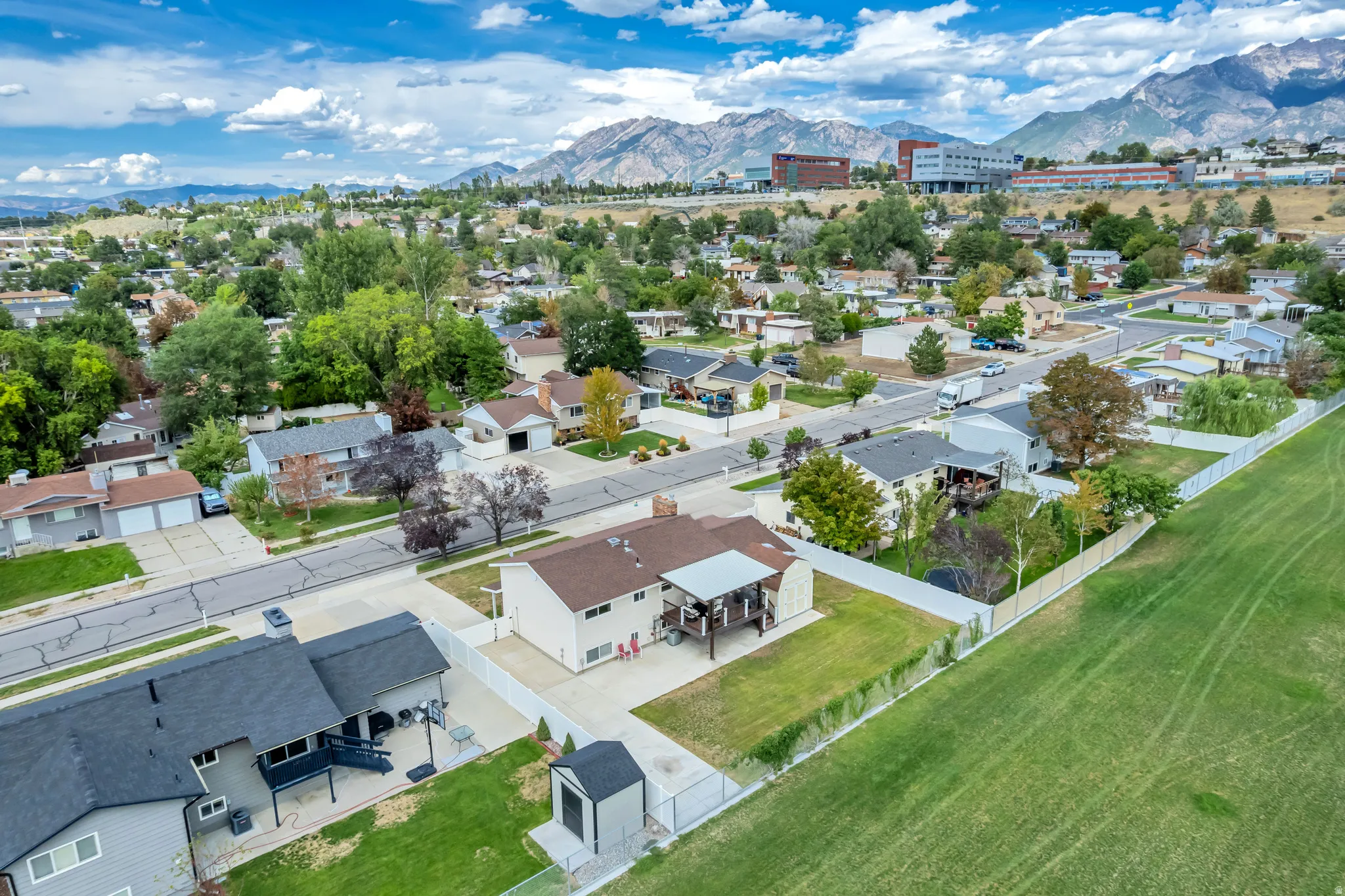 Expansive green space bordering the property, white perimeter fencing, multi-level deck with covered portion, storage shed, and mature trees