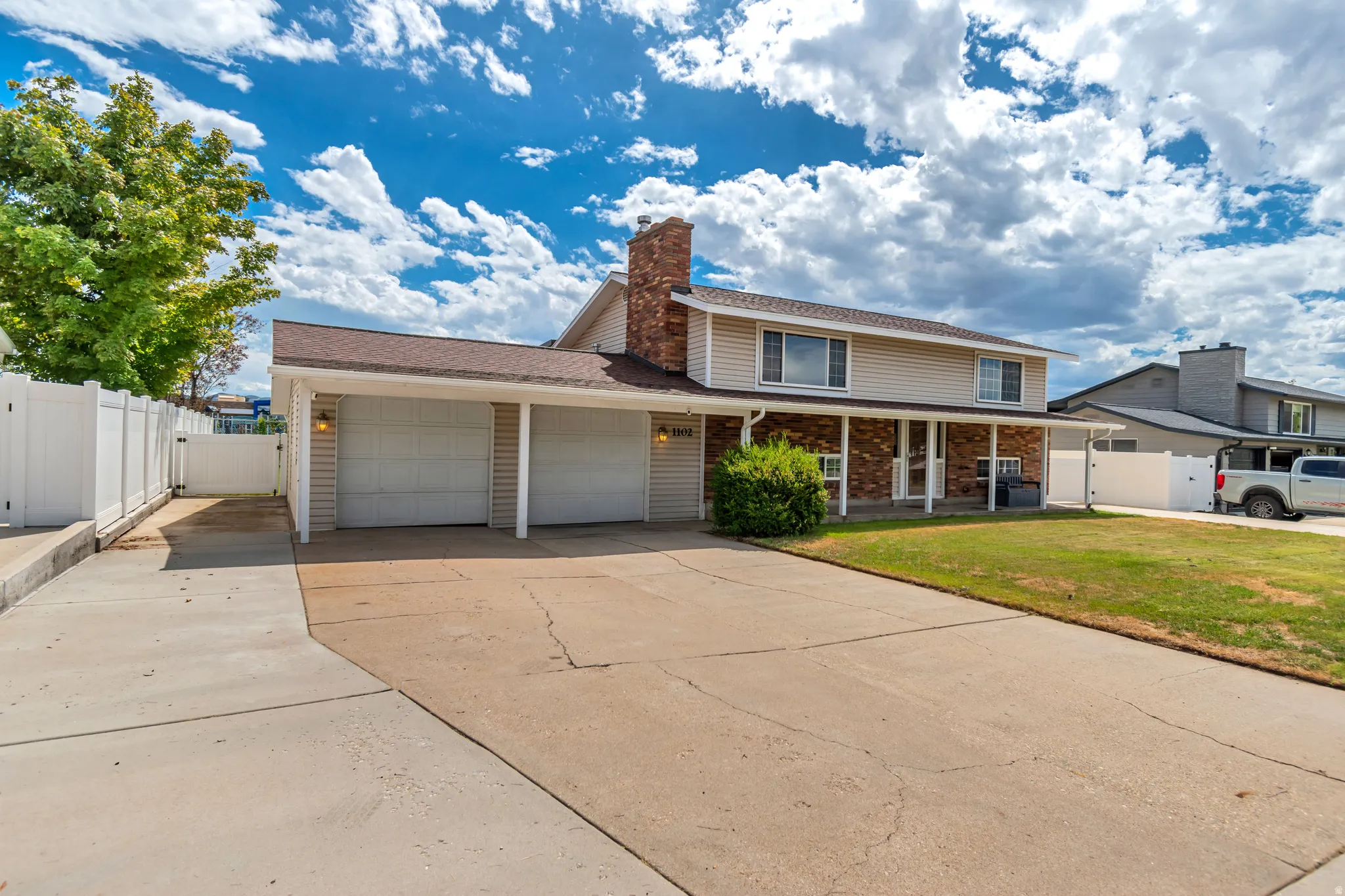 Two-car garage with individual doors, brick accent siding, covered front porch, and a white privacy fence