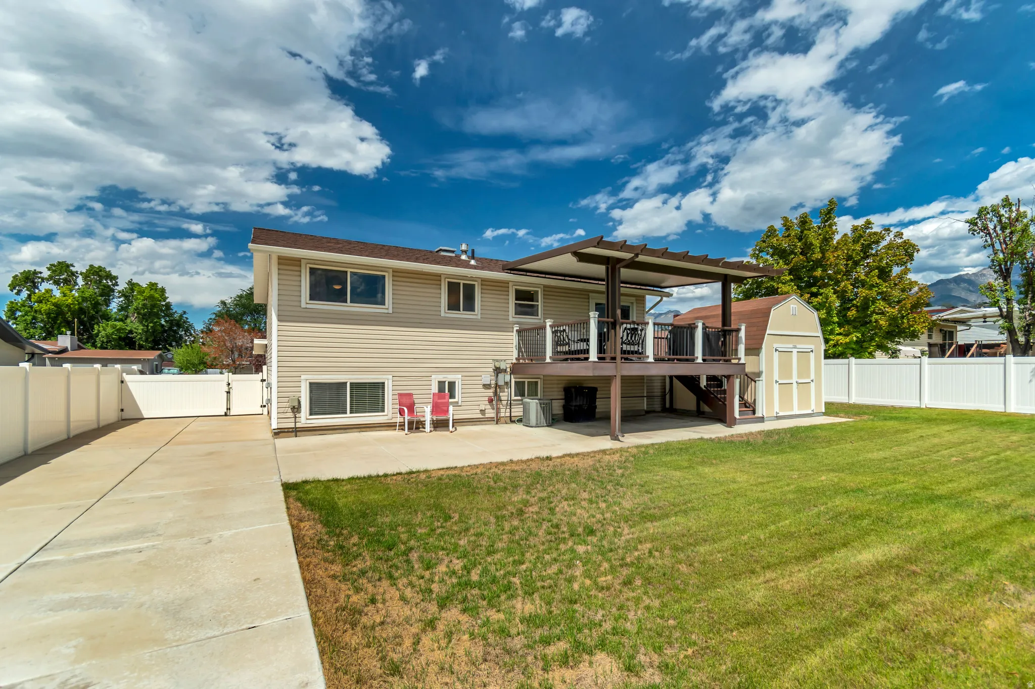 Expansive lawn area with a multi-level deck featuring a pergola, concrete patio, and a storage shed