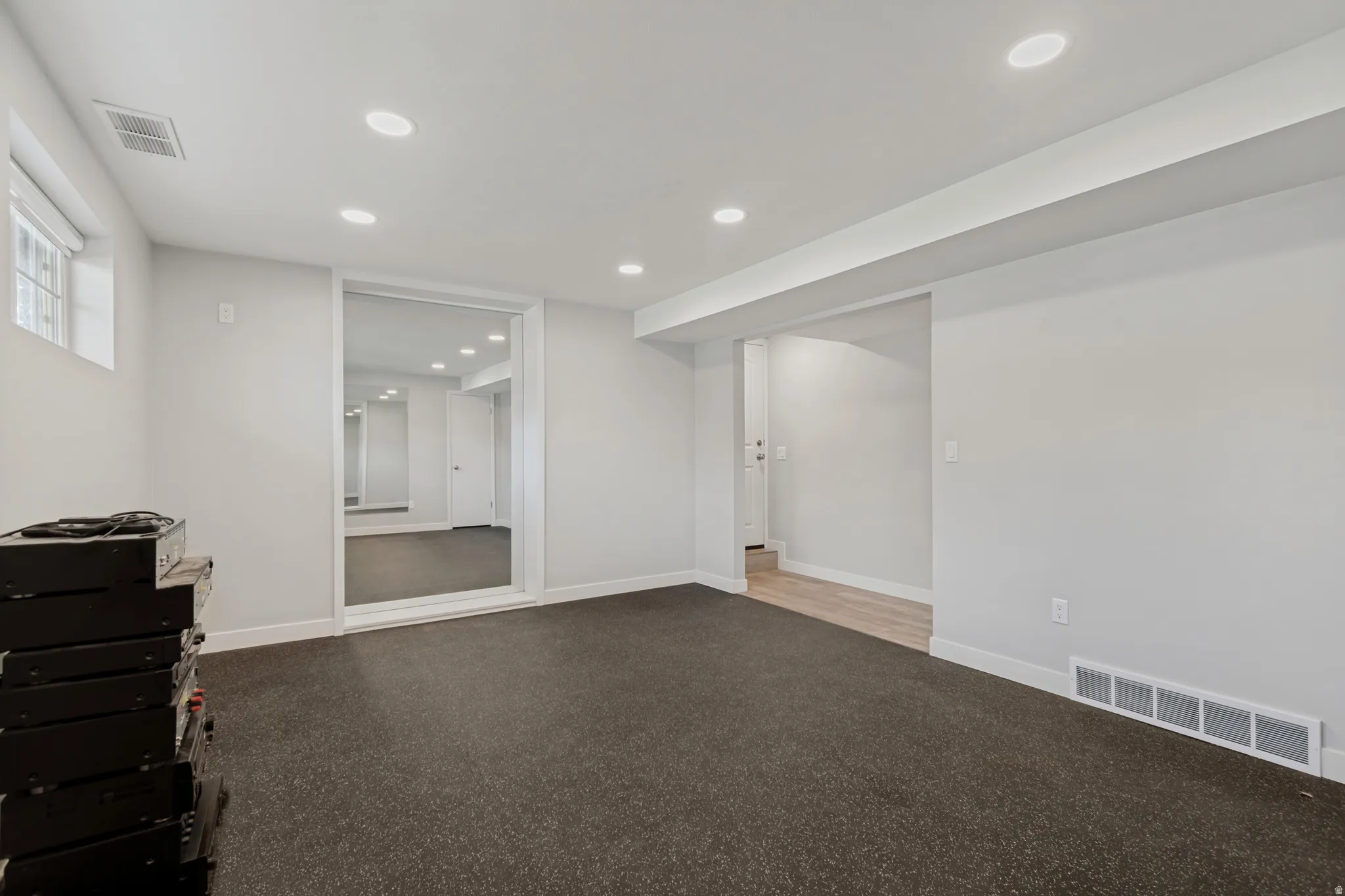 Recessed lighting with a flat white ceiling, light gray painted walls, dark gray flooring, a framed full-height mirror, and a window with a white frame