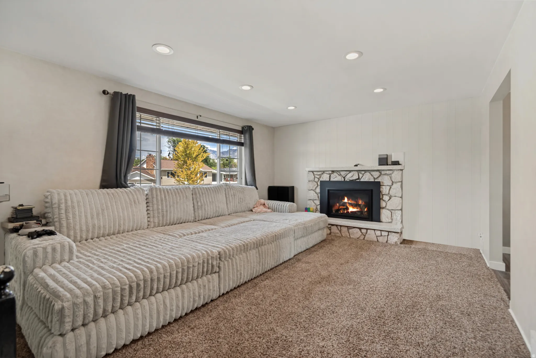 Stone-clad fireplace with a hearth, recessed ceiling lighting, textured wall paneling, and an expansive window