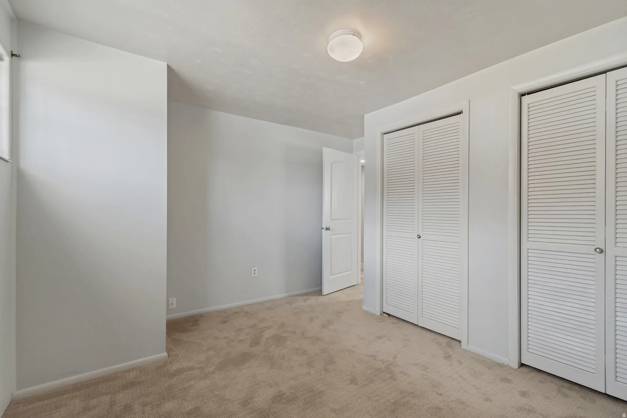 Light-colored carpeted flooring, white walls, two sets of louvered bifold closet doors, and a flush-mount ceiling light fixture