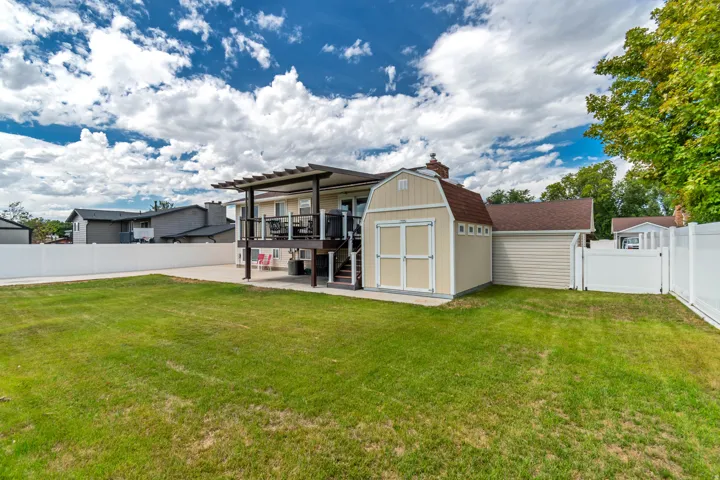 Expansive green space featuring a white vinyl fence, multi-level deck with pergola, and detached storage shed