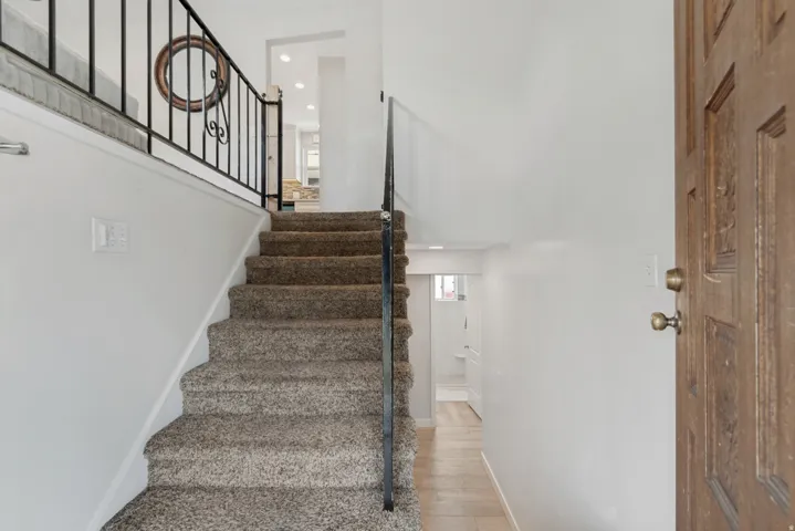 Carpeted staircase with wrought iron railing, leading to an upper level with recessed lighting