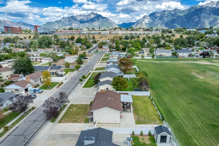 Expansive mountain range backdrop, residential neighborhood with paved streets, adjacent to a large grassy field, and a property featuring a separate outdoor storage shed