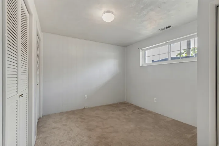 Wall-to-wall carpeting, multiple louvered bifold closet doors, and recessed window