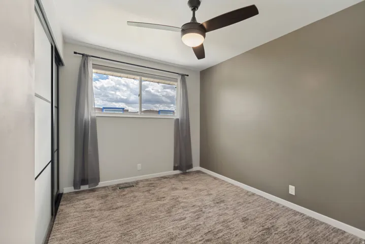 Carpeted room featuring a ceiling fan with integrated lighting, a large window, and sliding closet doors with dark framing
