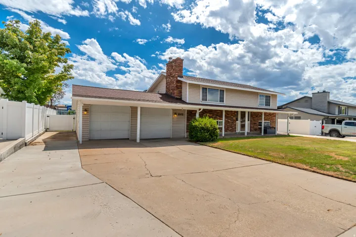 Two-car garage with individual doors, brick accent siding, covered front porch, and a white privacy fence