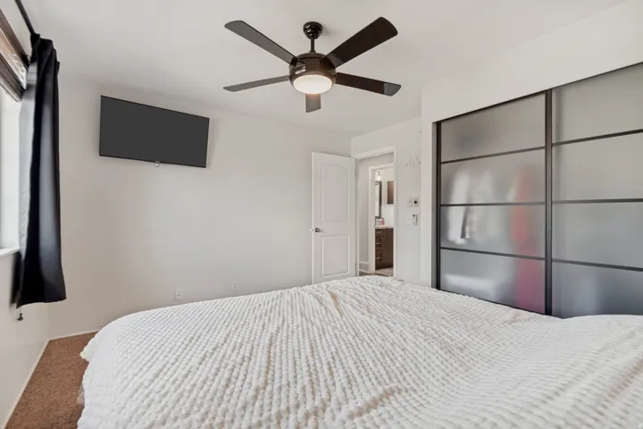 Recessed window with blinds, ceiling fan with integrated lighting, wall-mounted television, and sliding closet doors with frosted panels