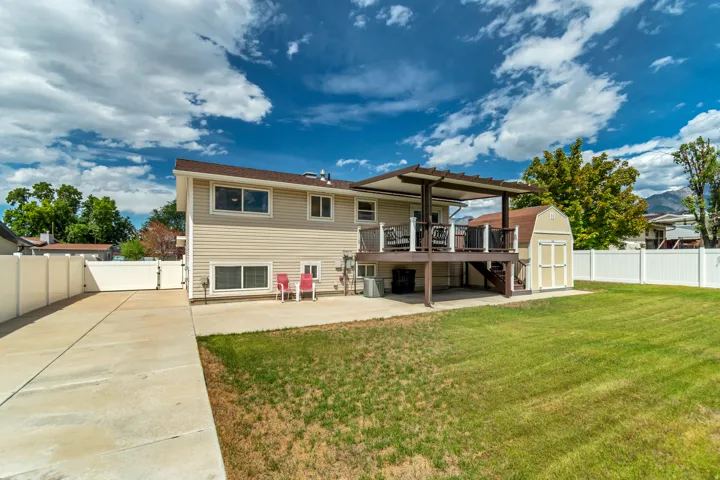 Expansive lawn area with a multi-level deck featuring a pergola, concrete patio, and a storage shed