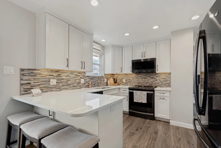 Contemporary kitchen featuring white cabinetry, a mosaic tile backsplash, wood-finish flooring, recessed lighting, and a breakfast bar