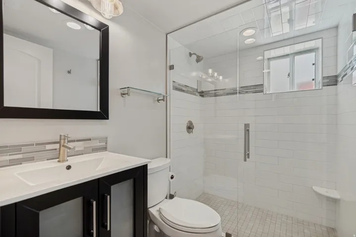 Glass-enclosed shower with subway tile surround and integrated shelving, vanity with white countertop and brushed nickel faucet, and mosaic tile backsplash