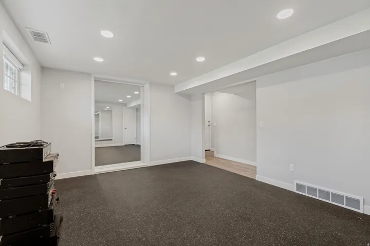 Recessed lighting with a flat white ceiling, light gray painted walls, dark gray flooring, a framed full-height mirror, and a window with a white frame