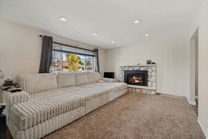 Stone-clad fireplace with a hearth, recessed ceiling lighting, textured wall paneling, and an expansive window