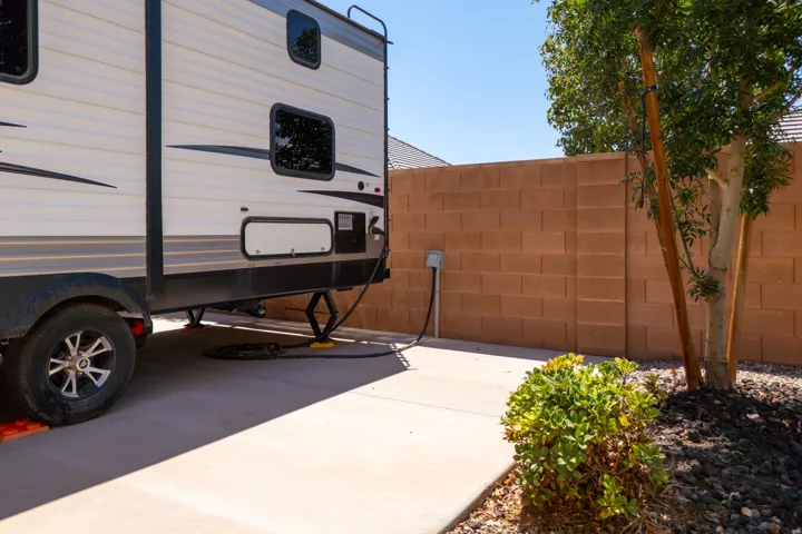 Paved hardscaping with an electrical hookup, bordered by a block wall and mature tree