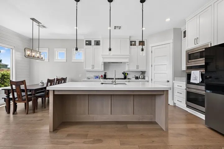 Spacious kitchen featuring an island with a built-in sink, stainless steel appliances, white cabinetry, and wood-finish flooring