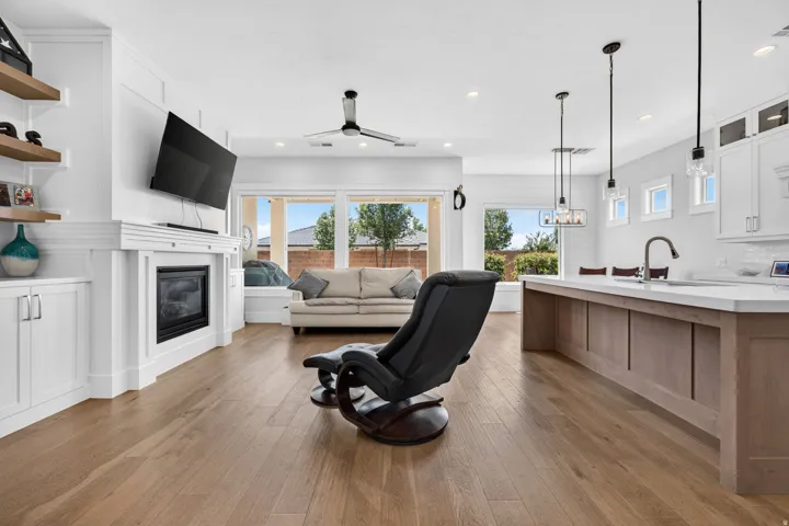 Wood-finish flooring throughout, built-in fireplace with white mantel, custom built-in cabinetry with floating shelves, kitchen island with solid surface countertop, and pendant lighting