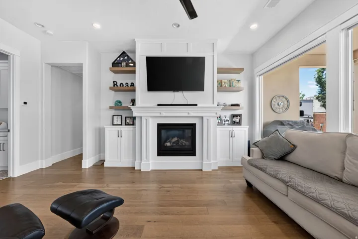 Hardwood flooring, built-in fireplace, white mantel, built-in cabinetry, and floating shelves