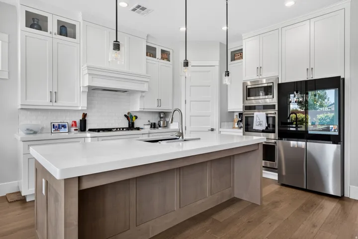 White shaker-style cabinetry with upper glass-front cabinets, a subway tile backsplash, a stainless steel appliance suite, wood-finish flooring, and a large center island with a light-toned countertop