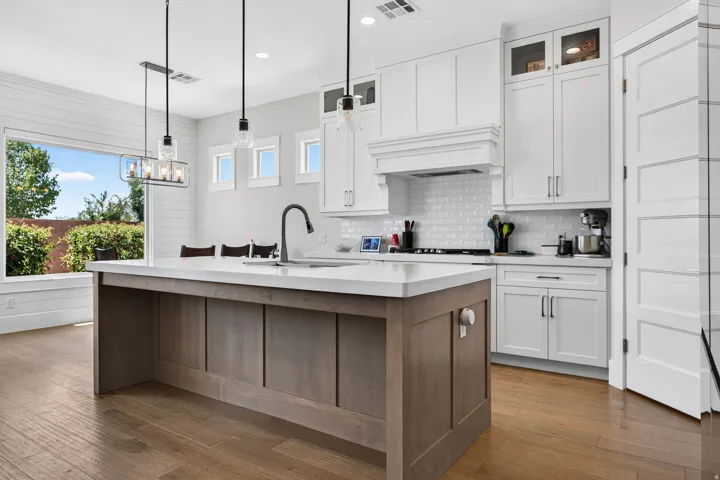 Gourmet kitchen featuring a central island with countertop, white shaker cabinetry, subway tile backsplash, and wood-finish flooring