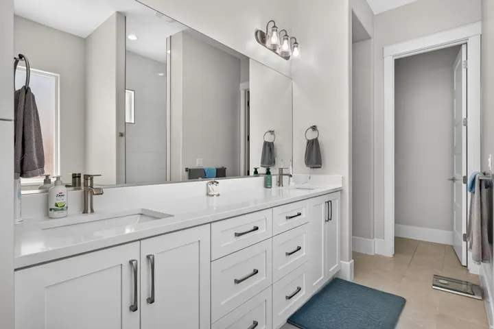 Dual undermount sinks with brushed nickel faucets, white cabinetry, integrated oversized mirror, and a four-bulb vanity light fixture