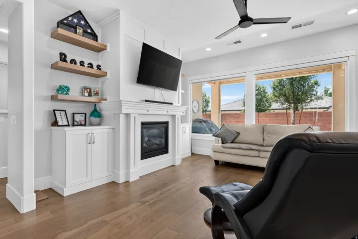 Built-in gas fireplace with mantel, wood-finish flooring, recessed lighting, ceiling fan, and large windows