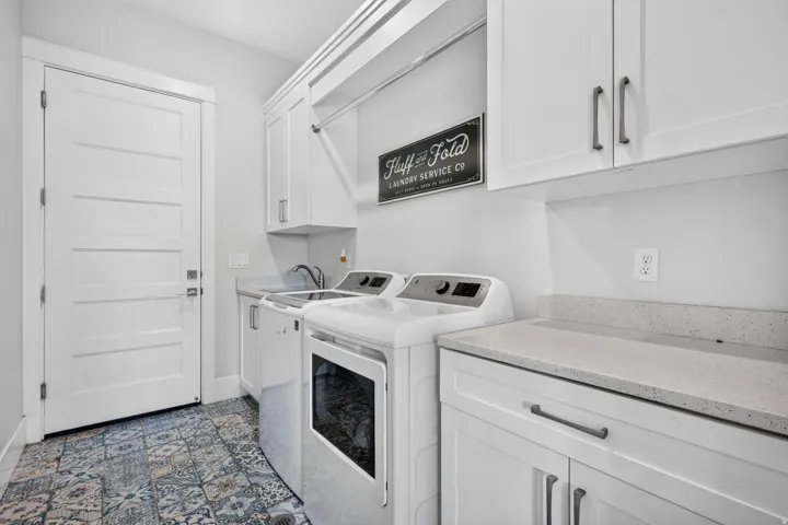 White shaker cabinetry, patterned floor tile, light-toned countertop, and a utility sink