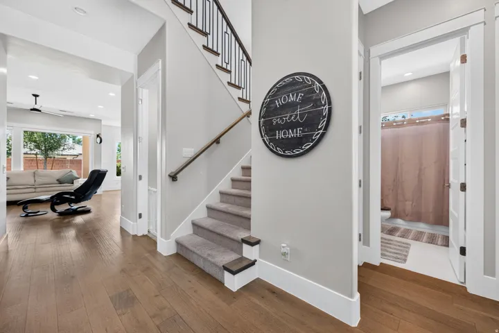 Wood-finish flooring throughout, carpeted staircase with dark wood treads and a metal spindle railing, and a ground-level bathroom with white tile flooring